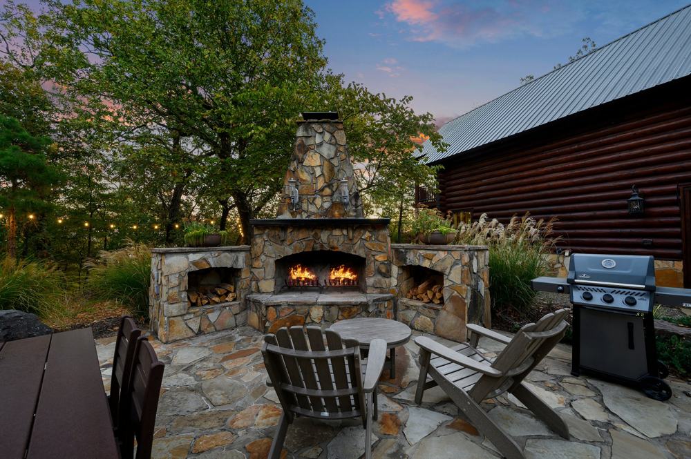 Outdoor stone fireplace with Adirondack chairs and grill at dusk