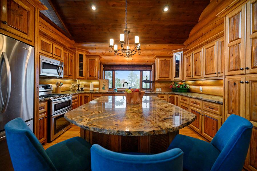 Kitchen with granite island, blue chairs and forest views